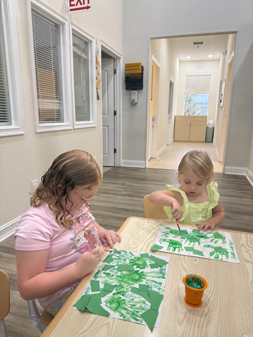Two children painting handprint crafts at the activity table at Ellie's World PPEC in Port Charlotte, Florida