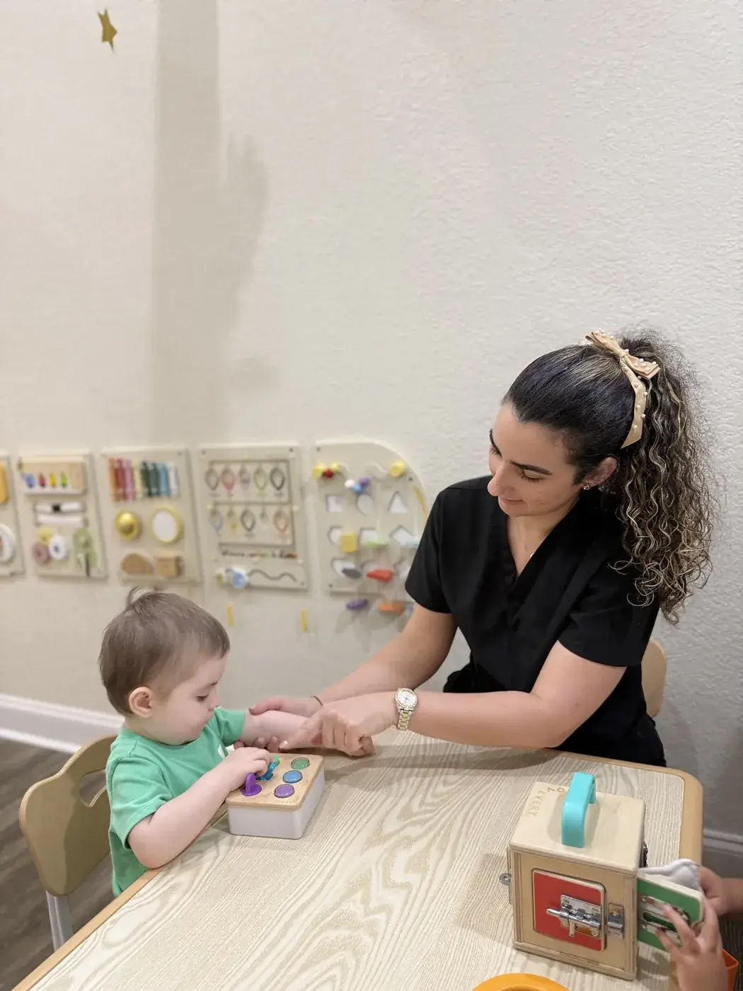 A staff member guiding a toddler through a fine motor activity at Ellie's World PPEC in Port Charlotte, Florida