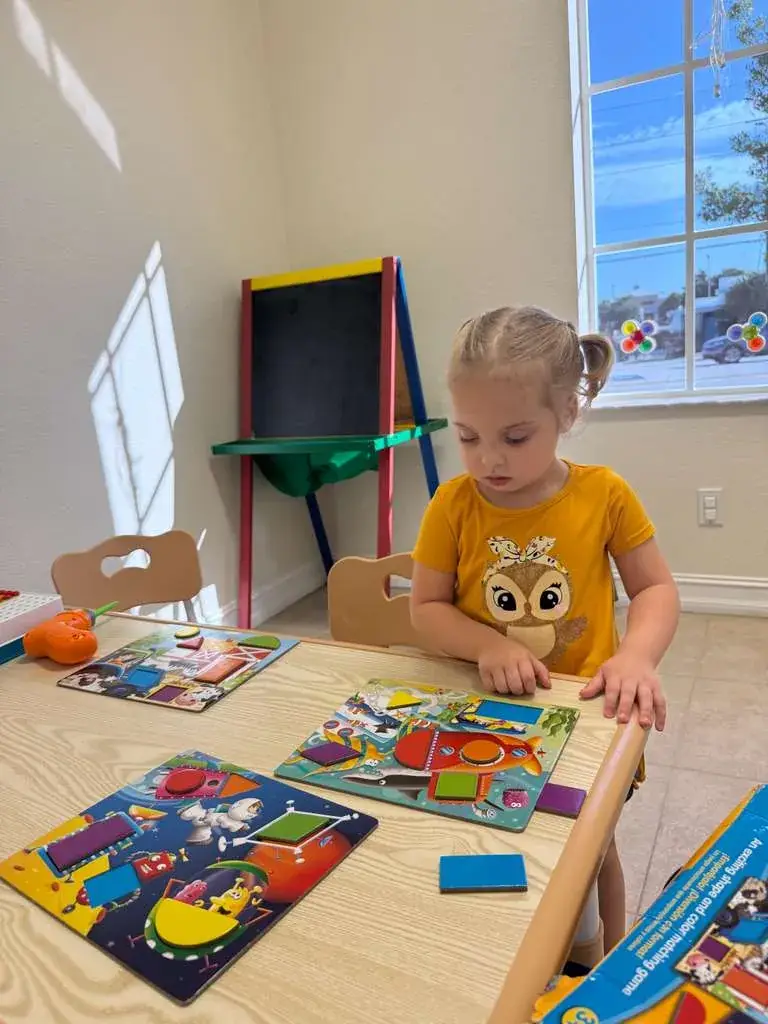 A girl working through matching puzzles at a child-sized table at Ellie's World PPEC in Port Charlotte, Florida