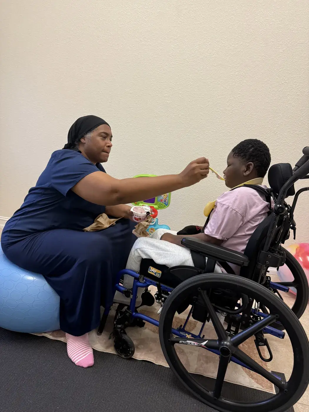 A nurse feeding a child seated in a wheelchair during lunch at Ellie's World PPEC in Port Charlotte, Florida
