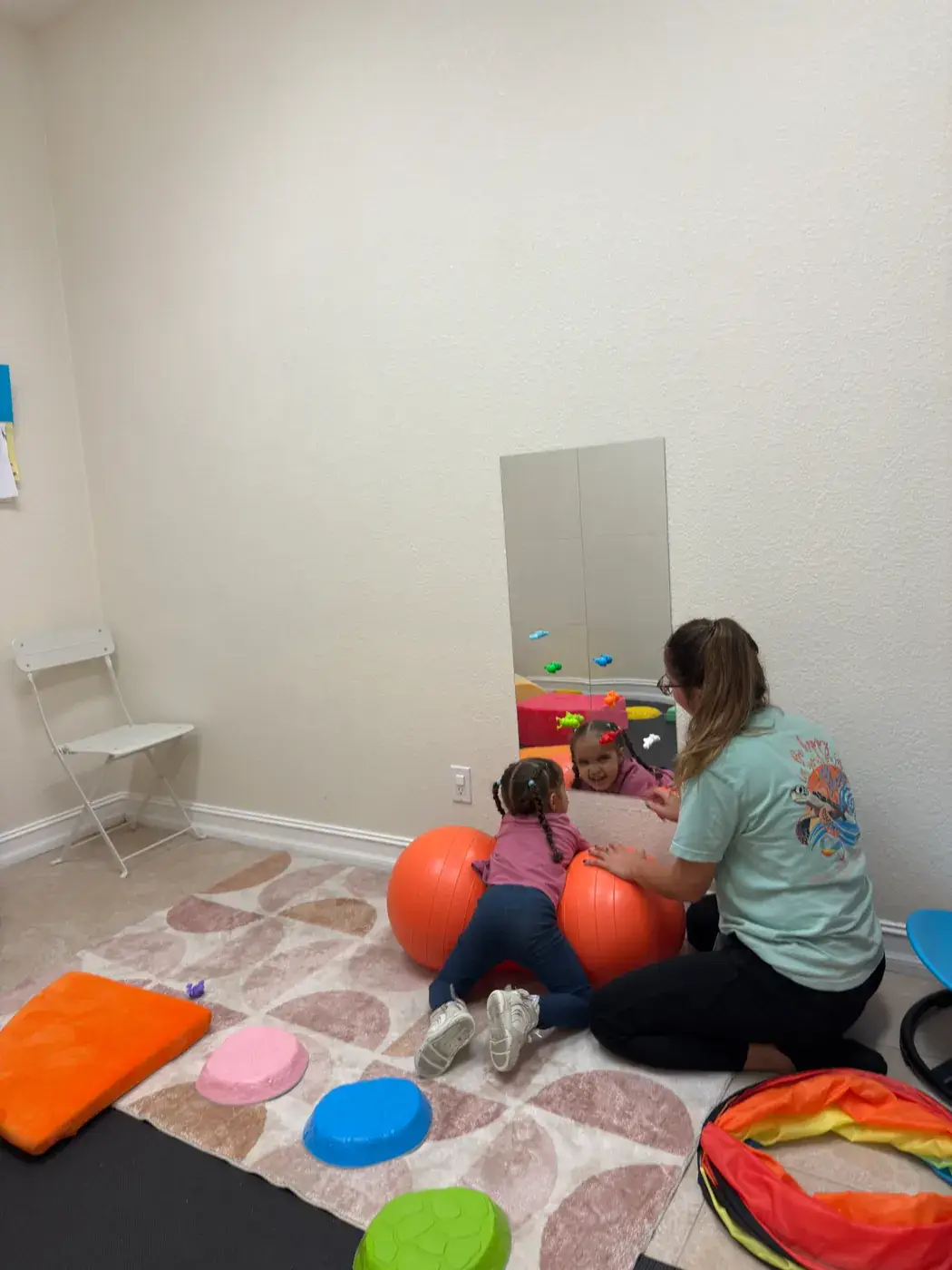 A therapist and a child working in front of a mirror in a therapy room at Ellie's World PPEC in Port Charlotte, Florida