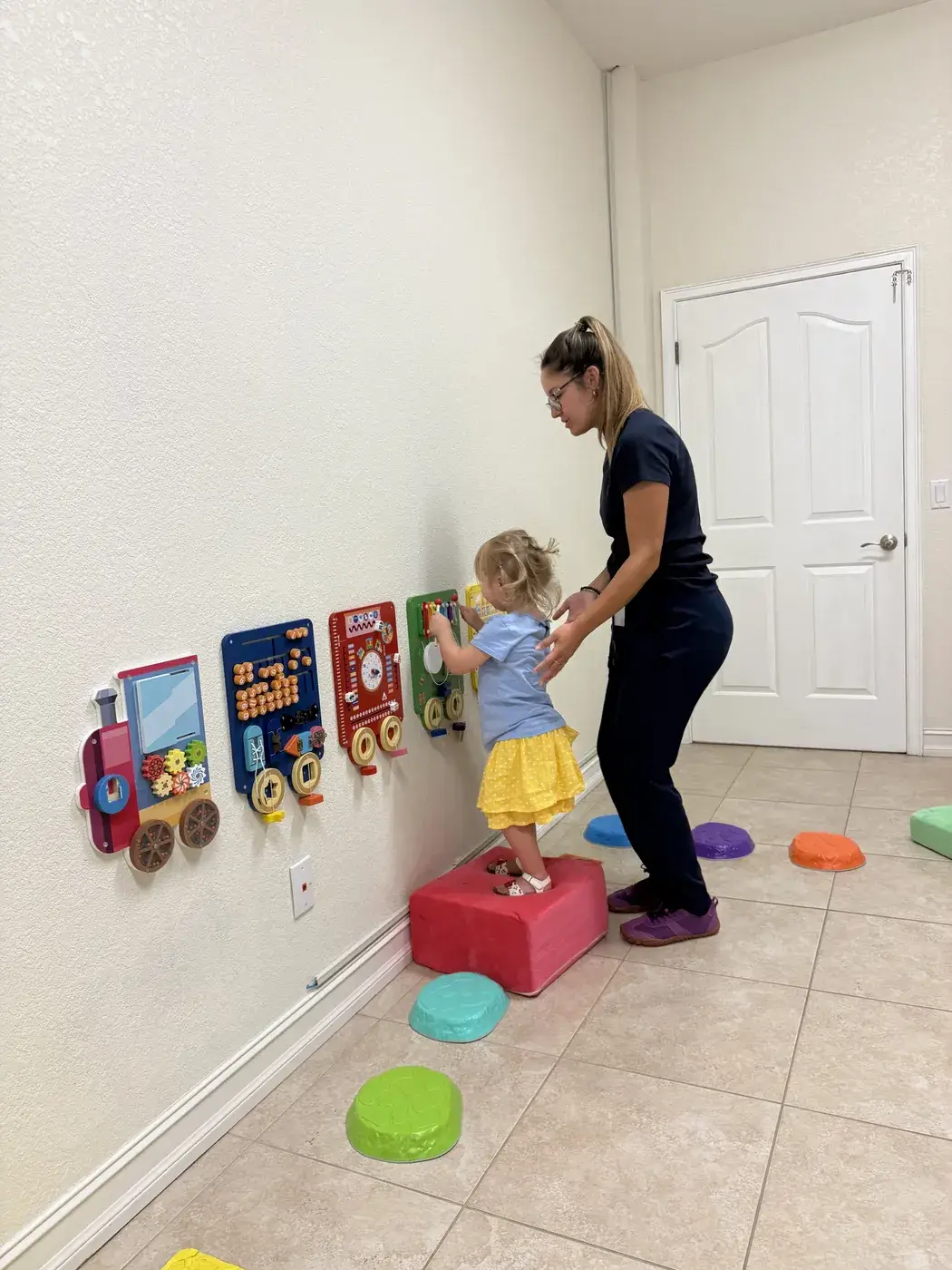 A therapist steadying a toddler stepping across balance pads at Ellie's World PPEC in Port Charlotte, Florida